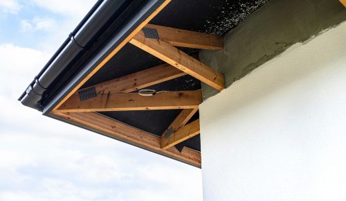 A newly applied layer of white silicone plaster on the wall of the house, visible roof trusses and a A newly applied layer of white silicone plaster on the wall of the house, visible roof trusses and a