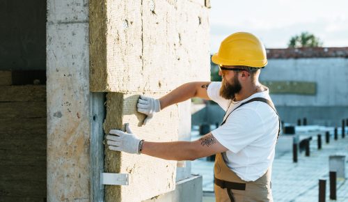 builder in protective helmet and googles doing insulation of wall at construction site builder in protective helmet and googles doing insulation of wall at construction site
