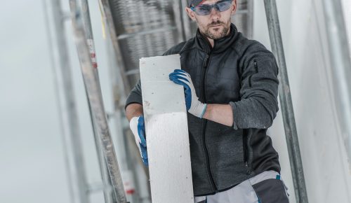 Caucasian Construction Worker Installing Insulation Material On Outside Walls Of House. Caucasian Construction Worker Installing Insulation Material On Outside Walls Of House.